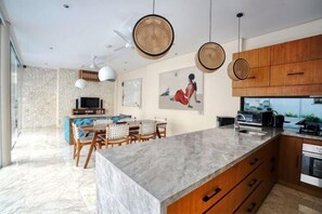A modern kitchen with a marble countertop, wooden cabinets, and a dining area with a TV and seating. - Beautiful Bali Villas (Bali)