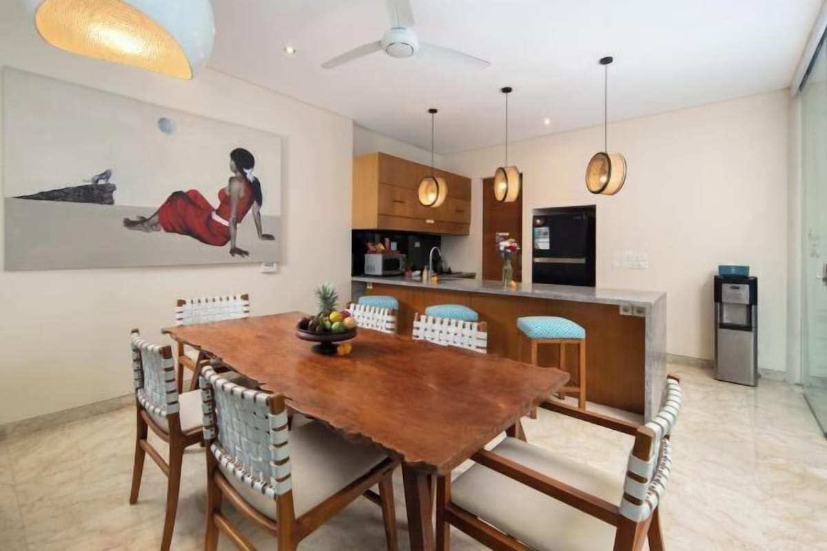 A dining area with a wooden table and chairs, a kitchen with wooden cabinets, and pendant lighting.