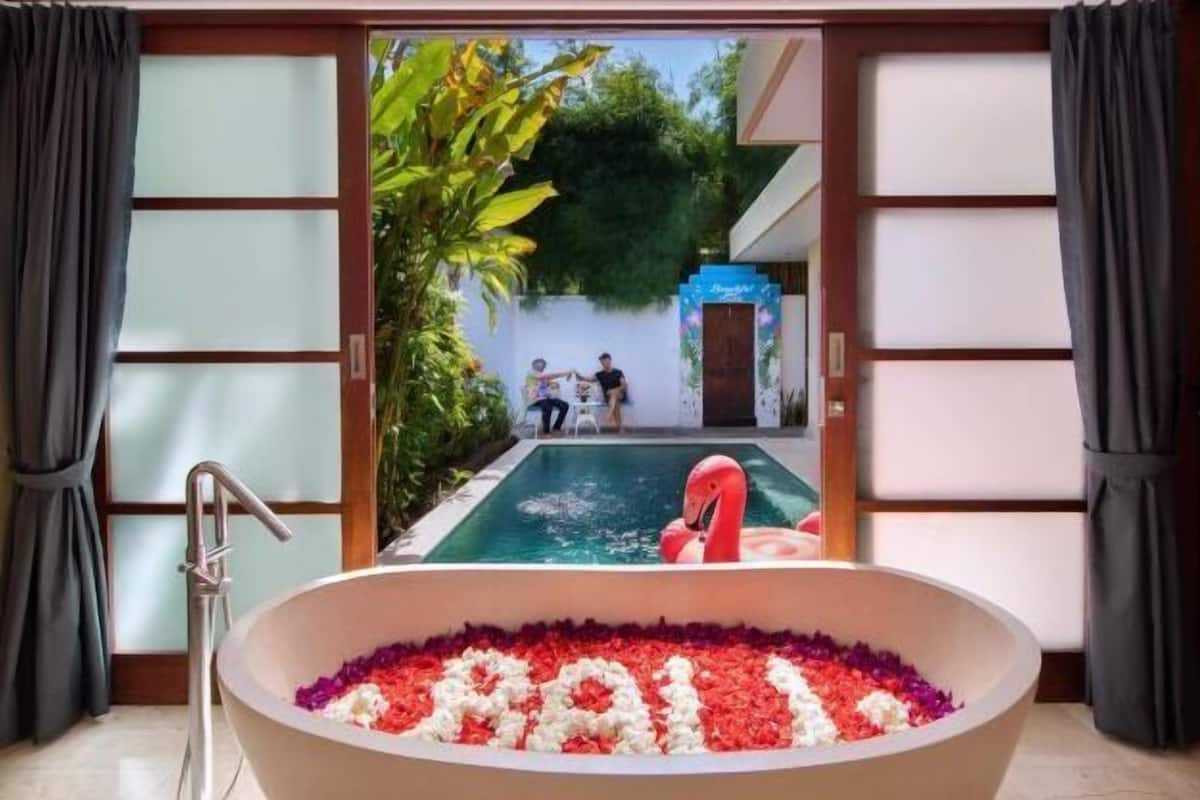 A bathtub filled with rose petals and a flamingo floatation device in a pool outside.