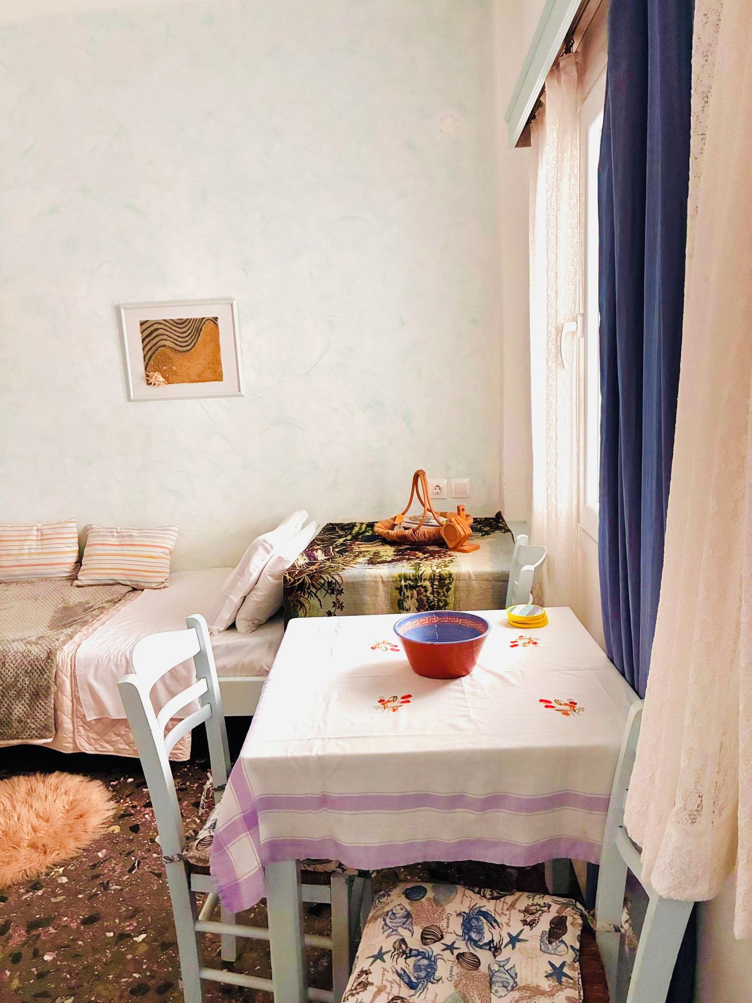 Een kleine kamer met een bed, een tafel met een kom en een kruik, een stoel, en een raam met gordijnen.