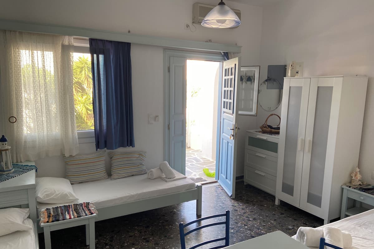A room with a bed, a bench, a table, a chair, a wardrobe, and a door leading outside.