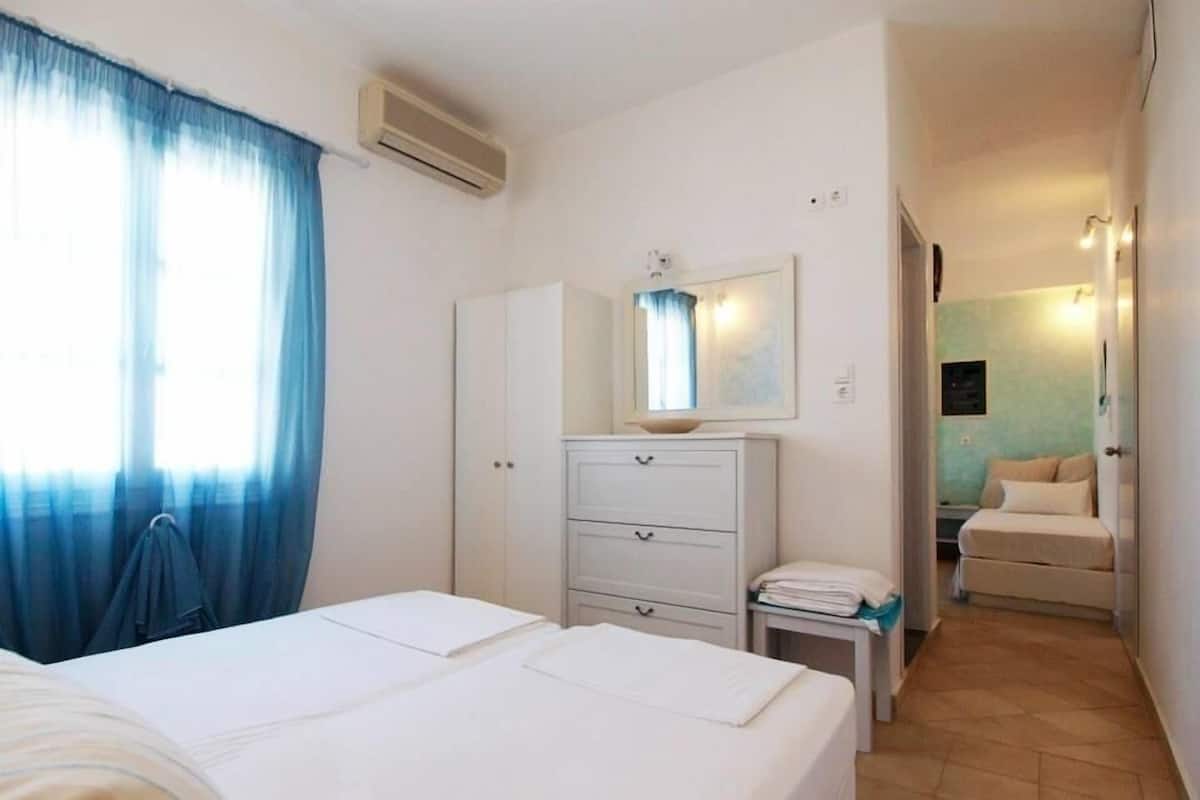 A hotel room with a bed, a bedside table, a dresser, and a bathroom visible through an open door.
