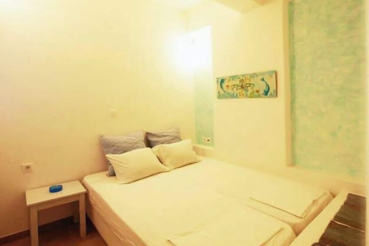 A small, simple room with a bed, a nightstand, and a wall-mounted painting.