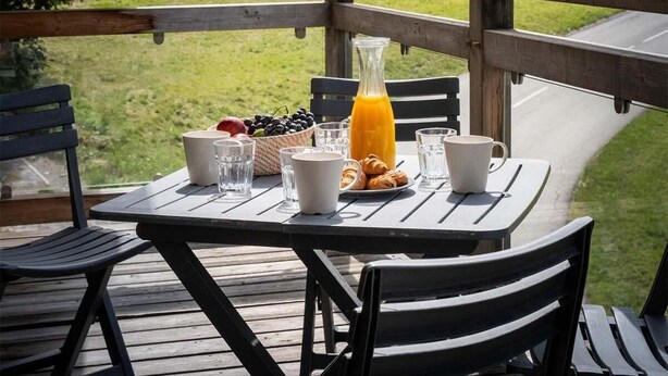 En träveranda med ett bord dukat för frukost, med utsikt över ett bergigt landskap.