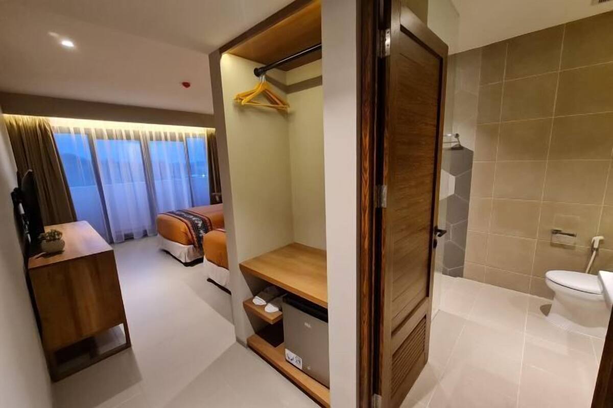 Ein modernes Hotelzimmer mit einem Holzbüro, einer Sitzecke mit einer Couch, einem kleinen Fernseher und einem Badezimmer mit Toilette und Dusche.
