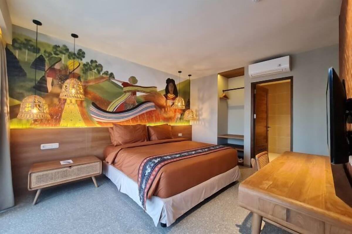 Ein Schlafzimmer mit einem Bett, einem Holztisch, einem an der Wand befestigten Fernseher und einem Wandgemälde.