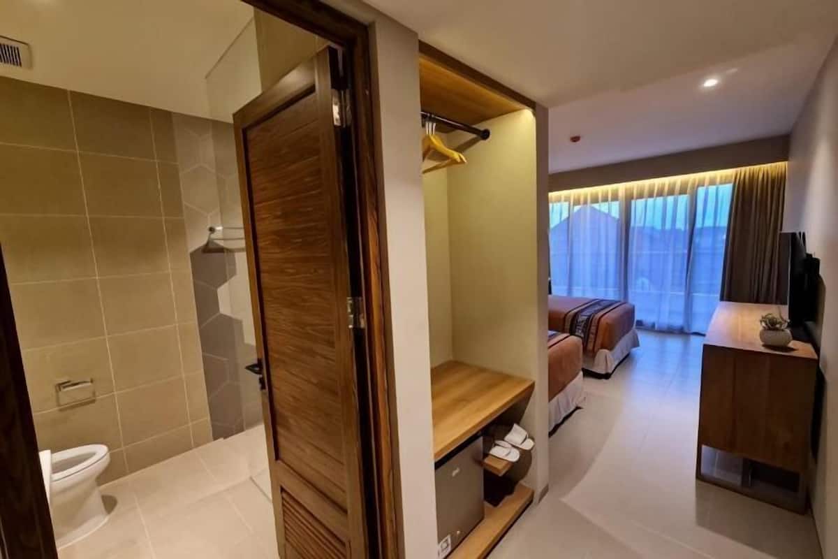 Ein Hotelzimmer mit Holztür, einem Badezimmer mit Toilette, einer Sitzecke mit Sofa und Fernseher sowie einem Holztisch.