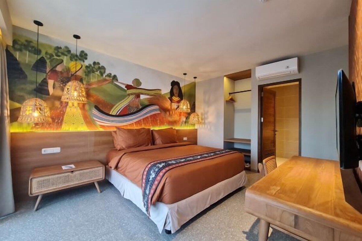 Een slaapkamer met een bed, een houten tafel, een wandtelevisie en een muurschildering.