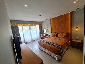 Een slaapkamer met een bed, een bureau, een stoel, een televisie en een raam met gordijnen.