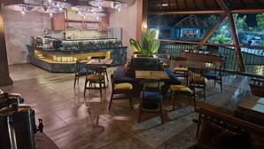 Un restaurante con barra, mesas y un amplio ventanal con vistas a un paisaje tropical.