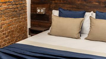 Een bed met een wit-blauwe spreidek en twee beige kussens, tegen een bakstenen muur.