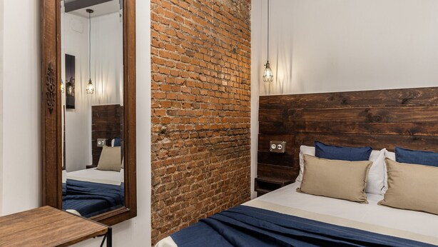 Een slaapkamer met een bakstenen muur, houten hoofdbord en een grote spiegel.