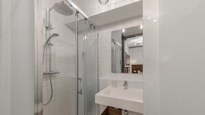 Een moderne badkamer met een douchecabine van glas, een wit wastafelmeubel en een spiegel erboven.
