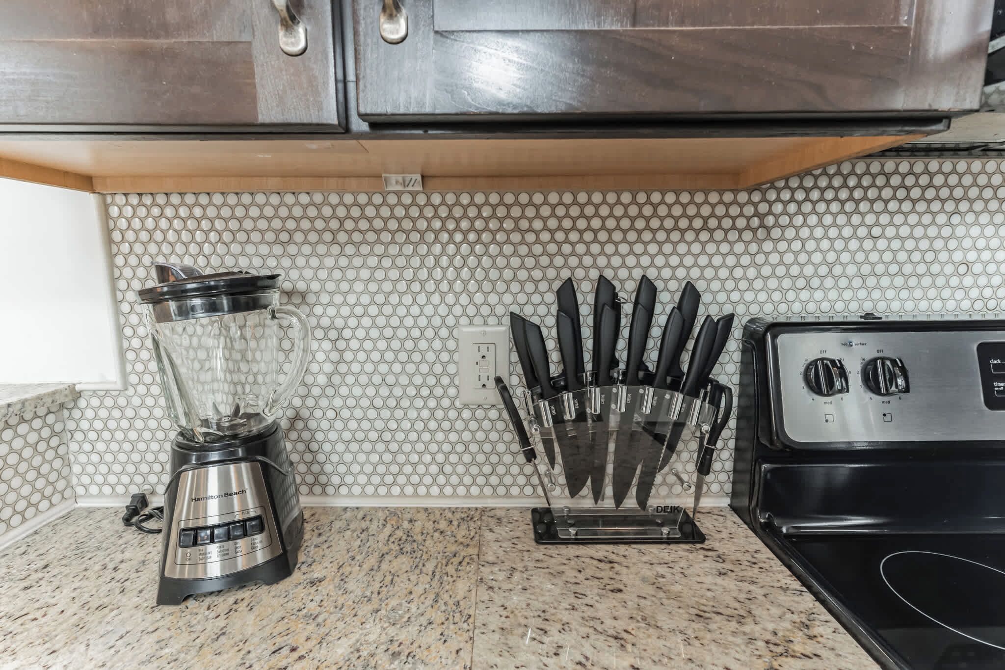 A kitchen with a granite countertop, a blender, a knife block, and a stove.