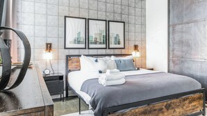 Ein modernes Hotelzimmer mit einem großen Bett, zwei Nachttischen, einer Holzbank und gerahmten Stadtansichten an der Wand.