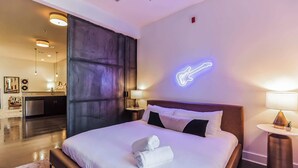 Moderni hotellihuone, jossa on siististi pedattu sänky, neonvaloilla koristeltu kitaran muotoinen kyltti ja miellyttävä, hyvin valaistu tunnelma.
