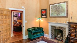 Ein Zimmer mit einem grünen Samtsofa, einem Kamin, einer Karte an der Wand und einer Holztür mit Gittermuster.