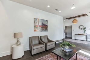 A modern living room with a sofa, a coffee table with a plant, a lamp, and a painting of a cityscape. - 1 BDR Loft close to Vanderbilt Hospital (Nashville)