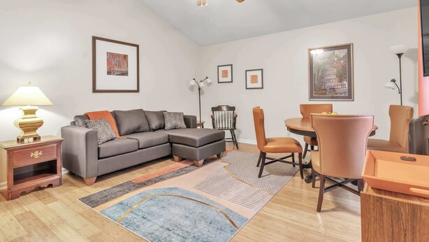 En moderne stue med en hjørnesofa, et spisebord med stole, en loftventilator og billeder i rammer på væggene.