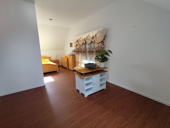 A bedroom with a wooden bed, a nightstand, a dresser, and a large window. - Vacation cottage SWD (Schweigen-Rechtenbach)