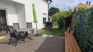 Eine Terrass mit Tisch, Stühlen, einem Grill und einem grünen Sonnenschirm.