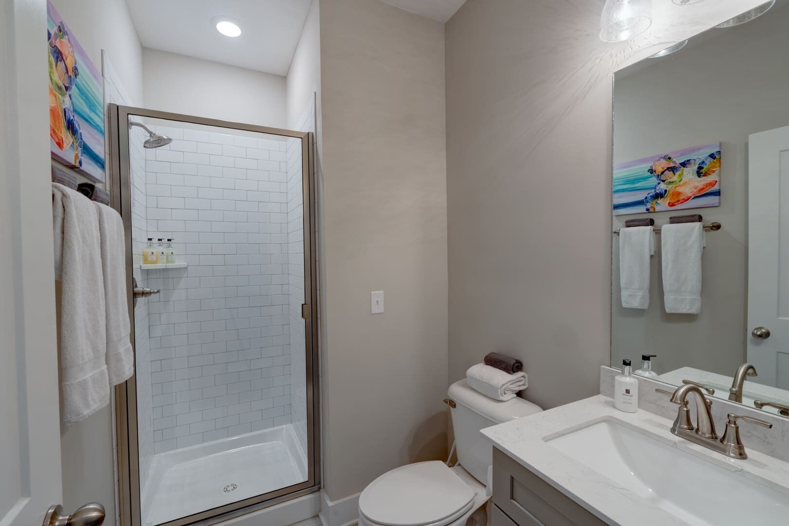 A modern bathroom with a glass-enclosed shower, white tiled walls, a toilet, and a sink with a mirror.