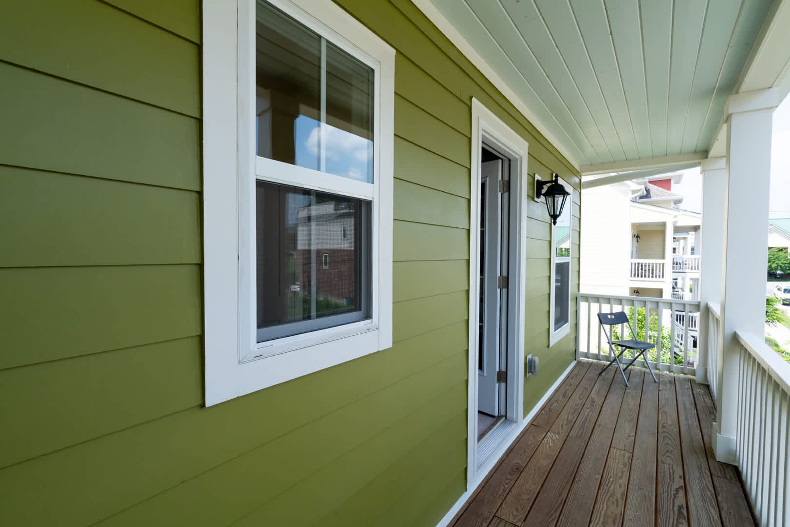 A green exterior with a wooden deck, a window, and a door.