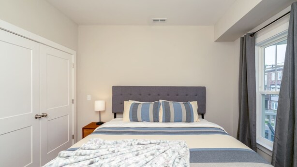Une chambre d’hôtel avec un lit, une table de chevet, une lampe et une fenêtre avec des rideaux.