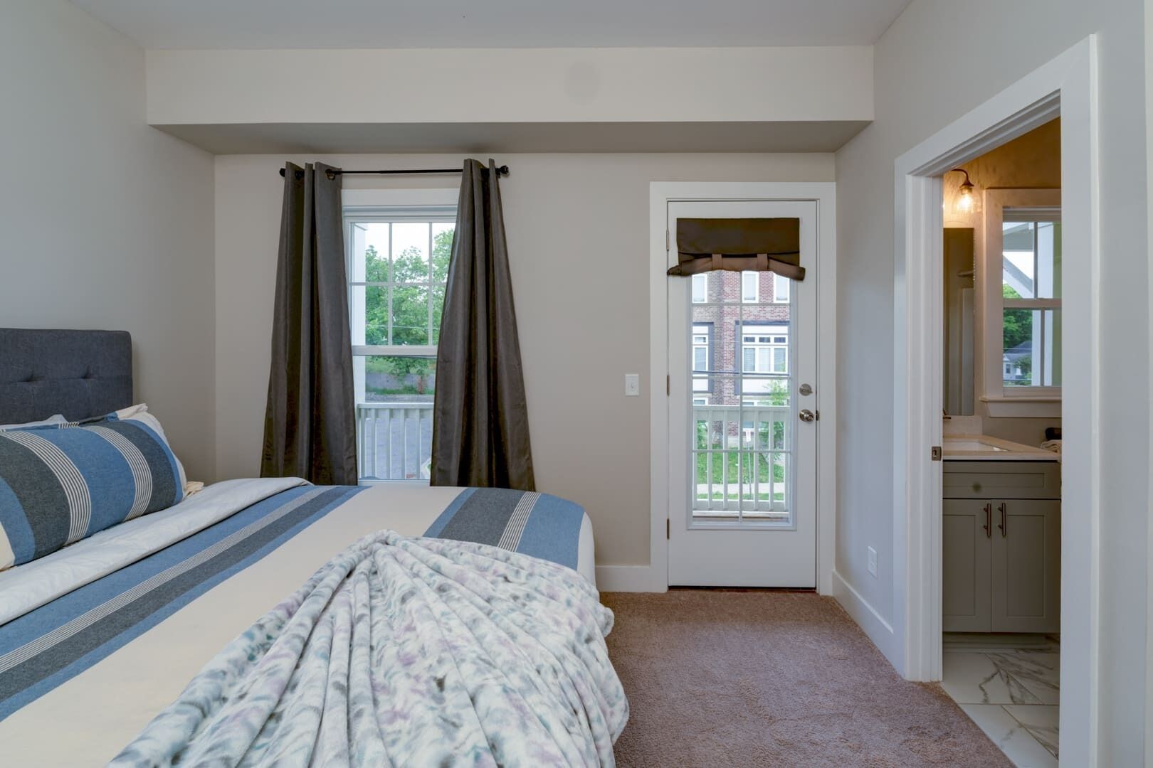 A bedroom with a bed, a door leading to a balcony, and a bathroom visible through an open door.