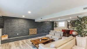 Un salon moderne avec un mur en briques sombres, une table basse en bois, un canapé beige et un fauteuil à motifs.