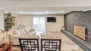 Un salon moderne comprenant un canapé, une table à manger avec des chaises, une cheminée et un téléviseur fixé au mur.