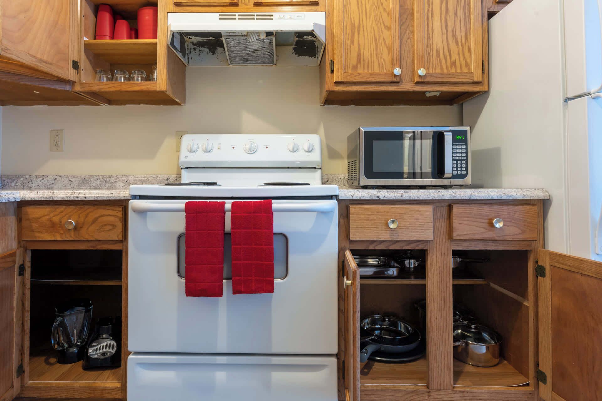 Una cocina con armarios de madera, una estufa blanca, un microondas y una licuadora.