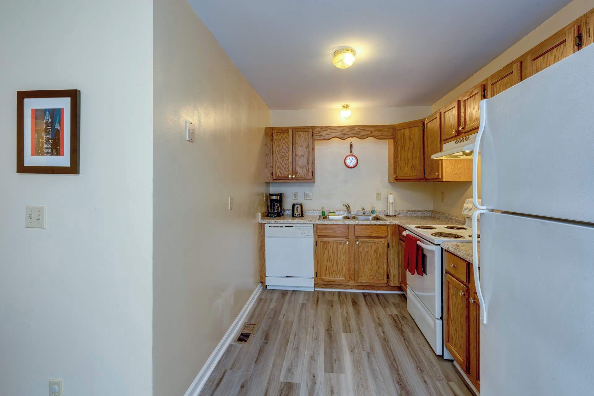 Una cocina compacta con armarios de madera, un refrigerador blanco, estufa y lavavajillas.