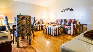 Ein Wohnzimmer mit Holzboden, einem floralen Sessel, einem gestreiften Sofagarnitur und einem Deckenventilator.