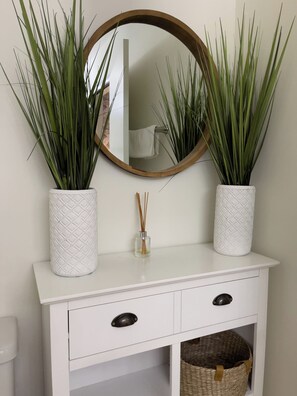 Bathroom features a vanity with a countertop, two plant vases, a round mirror, a drawer, and a wicker basket.