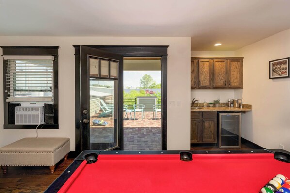 A pool table in a room with a sliding glass door leading to an outdoor patio with chairs and a table.