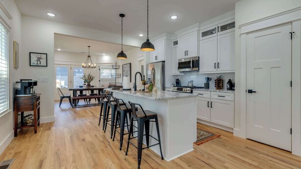 Cocina moderna con armarios blancos, una isla central con taburetes de bar, electrodomésticos de acero inoxidable e iluminación colgante.