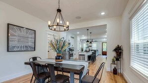 Una cocina moderna con electrodomésticos de acero inoxidable, una mesa de comedor de madera con taburetes de bar y una araña.