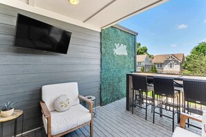 A modern outdoor seating area with a TV mounted on the wall, a decorative wall with 'Hello Nashville' text, and a view of residential buildings.