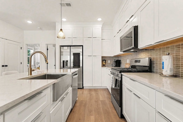 A modern kitchen with white cabinetry, stainless steel appliances, and a wooden floor.