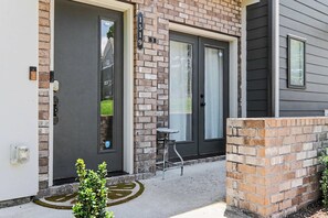 A residential building with two dark-colored doors, a brick wall, and a small outdoor seating area.