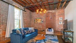 A room with a blue sofa, a white chair, a wooden coffee table, and a brick wall. - Stellar Condo | Sleeps 4 | 10 mins from Broadway! (Nashville)