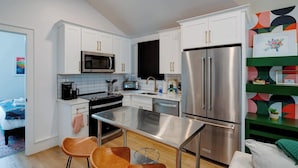 A modern kitchen with white cabinets, stainless steel appliances, and a bar area with stools. - Stylish Modern Bungalow in Nashville's 12 South (Nashville)