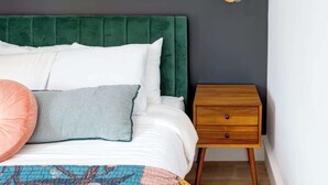 A bedroom with a green upholstered headboard, a wooden nightstand with drawers, and a wall-mounted light fixture. - Stylish Modern Bungalow in Nashville's 12 South (Nashville)