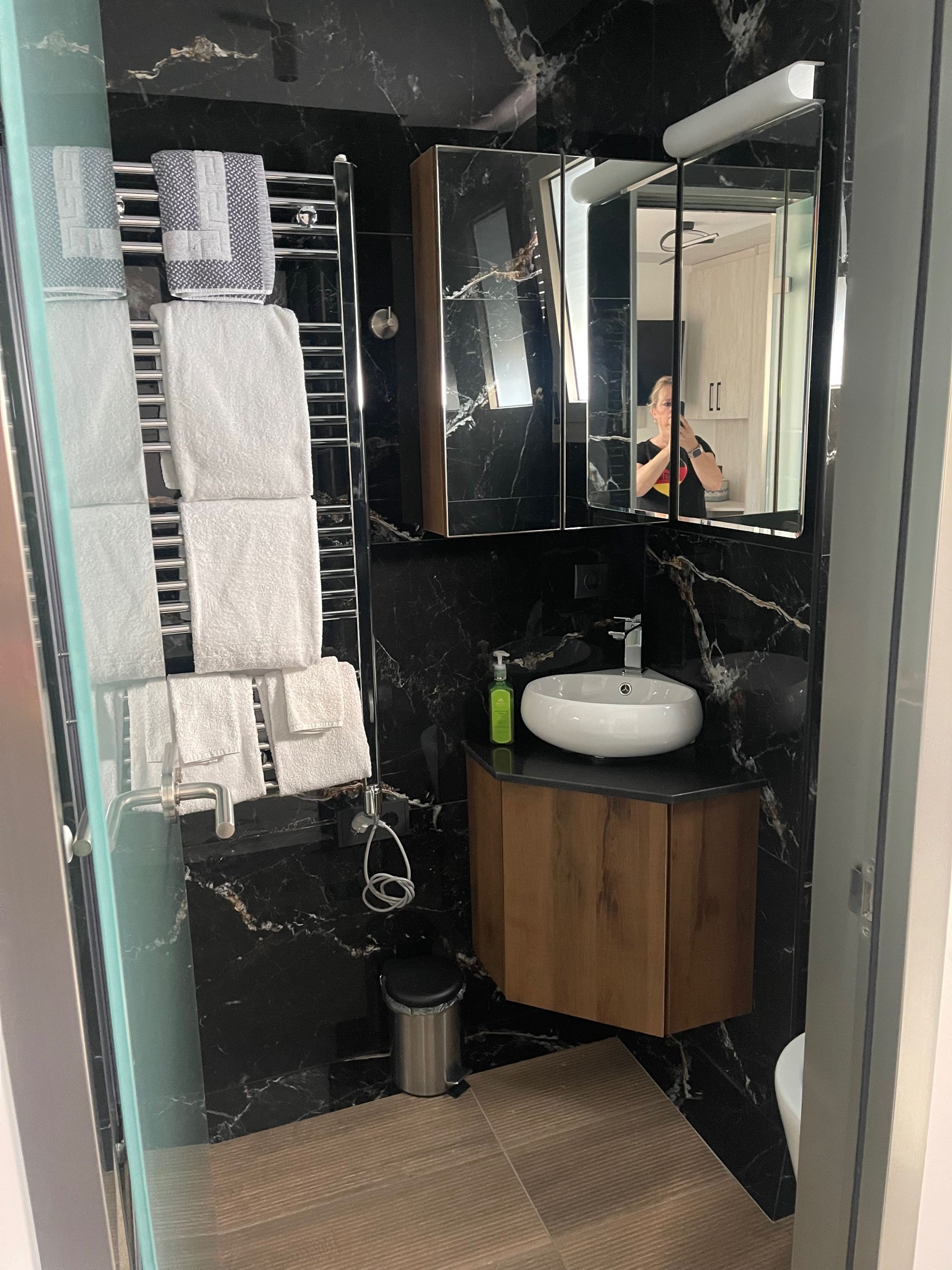 A modern bathroom with a black marble wall, a white sink, and a wooden vanity.