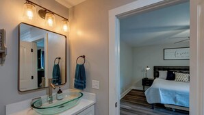 Un baño moderno con un lavamanos de cristal, un espejo grande y un perchero con dos toallas.