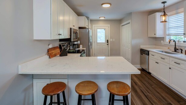 Una cocina moderna con armarios blancos, una isla grande con taburetes, microondas, refrigerador y lavavajillas.