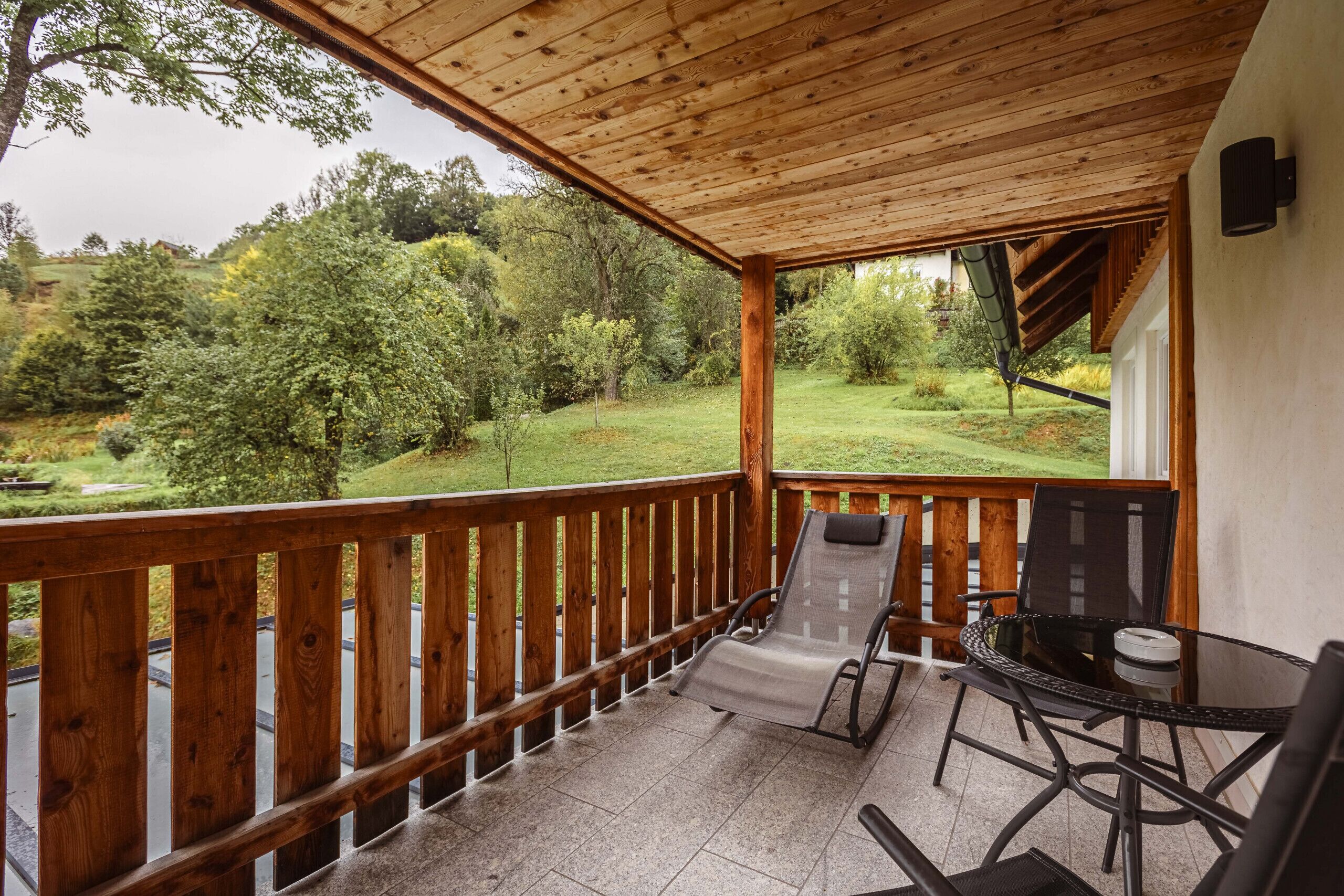A covered patio with a wooden railing, a table, and two chairs.