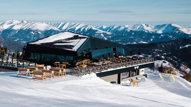 En modern hotellbyggnad i ett skidområde, med en fasad av glas, omgiven av snötäckta berg.