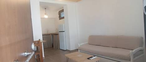 Un soggiorno moderno con soffitto in legno, un divano beige, un tavolino da caffè e una zona cucina sullo sfondo.